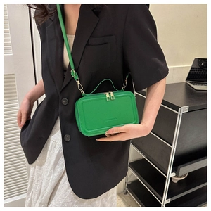 Close-up of green suitcase-shaped crossbody bag with dual metal zippers and handle