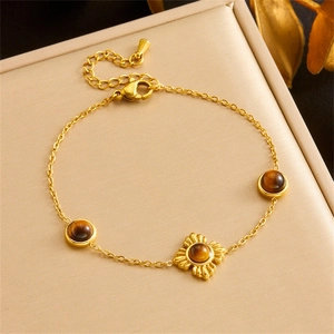 Detail of gold flower chain bracelet with brown tiger eye stone on beige jewelry cushion