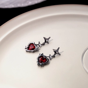 Detail of dark red heart zircon earring with black metal star on a beige ceramic plate