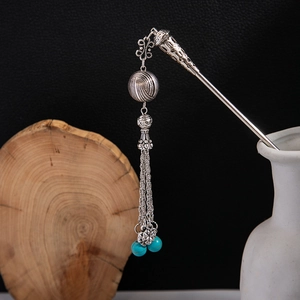 Detail of silver hair stick with turquoise beads and metallic tassels in a vase