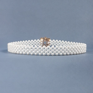Detail of elegant white pearl belt featuring a golden flower metal buckle and woven texture