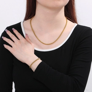 Set aus goldener Edelstahl-Box-Halskette und Armband getragen von einem Model auf Schwarz