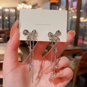 Detail of silver bow tassel earrings featuring dangling chains and zircon accents