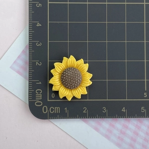 Macro shot of a 2.5cm yellow resin sunflower charm on a metric scale grid background