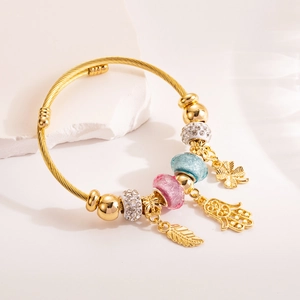 Gold beaded wire bracelet with Hamsa Hand and clover charms on a white stone background