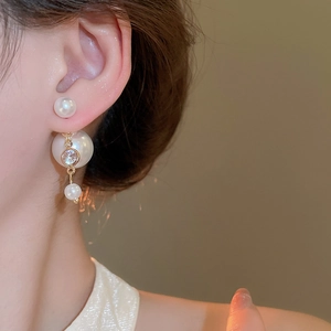 Detail of double-sided pearl earrings with gold accents and zircon on a female model