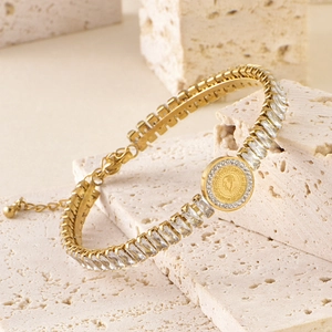 Detailed close-up of a gold-plated bracelet with baguette zircons and a relief coin charm