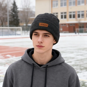 Thick dark grey winter knit beanie with leather patch shown on a model in snow