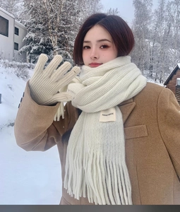 Outdoor shot of white knitted scarf and gloves paired with a brown wool coat in the snow