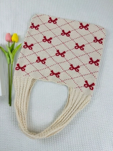 Detailed knit texture of beige tote bag with red bow pattern and thick cable strap