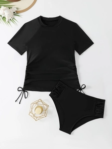 Flat lay of black two-piece tankini set with drawstring side ruching on beige background