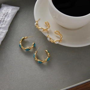 Detailed view of gold C-shape earrings with turquoise and pearl on a grey surface