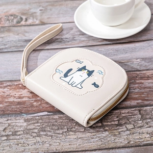 Short beige wallet with embroidered cartoon cat on a wooden table with a tea cup