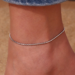 Close-up of minimalist silver stainless steel chain anklet worn on a woman's ankle
