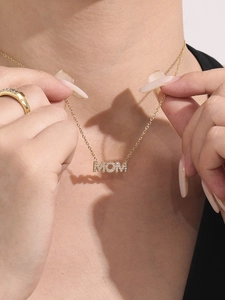 Close-up of golden MOM letter pendant necklace with cubic zirconia on elegant model