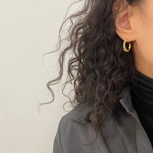 Close-up of golden twisted hoop earrings worn by a model with curly hair for a stylish look