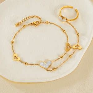 Detail of gold heart-shaped ring and bracelet set with white shell inlay on tray