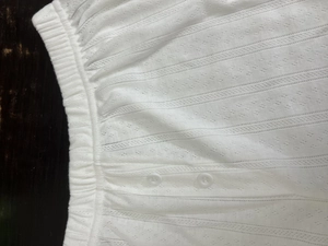 Détail d'un pyjama blanc en tricot avec texture jacquard ajourée et doubles boutons