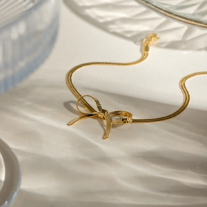 Macro detail of golden bow necklace with delicate snake chain and elegant glass reflection