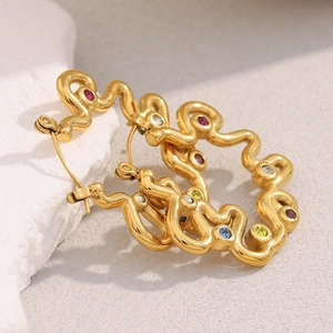 Detail of gold wavy earrings with colorful zircons set on a white stone background