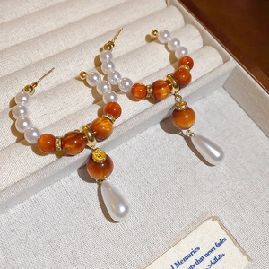 Detail view of elegant teardrop drop earrings with white pearls and orange resin beads