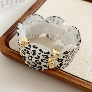 Detail of leopard print resin beads and golden metal spacers on a wide elastic bracelet