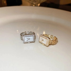 Macro shot of gold and silver watch-shaped rings with zircon crystals on white porcelain