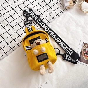 Detail of yellow canvas chest bag with 3D plush bear and white lettered strap