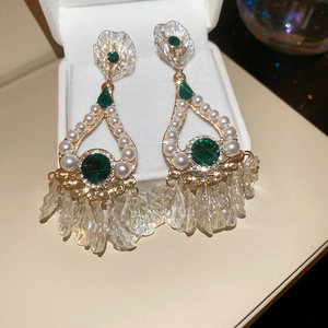Close-up of gold earrings with emerald green gems, pearls, and iridescent leaf tassels