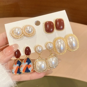 Set of five elegant gold earrings featuring pearls and red resin on a white display card