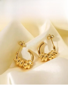 Détail des boucles d'oreilles en titane doré 18 carats sur fond de soie plissée