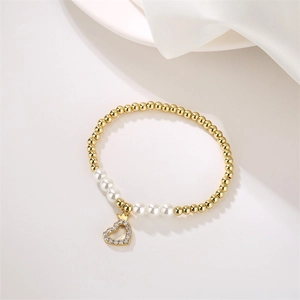 Detalle de pulsera de cuentas doradas y un colgante de corazón con corona