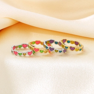 Detail of four colorful enamel heart rings on silk background with gold and silver bands