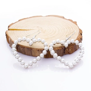 Detailed view of heart-shaped pearl drop earrings on a natural wood slice background