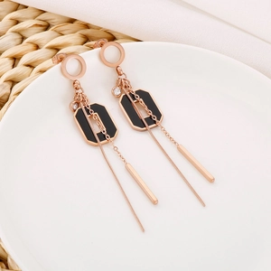 Détail macro de boucles d'oreilles pampilles or rose avec breloques noires sur assiette blanche