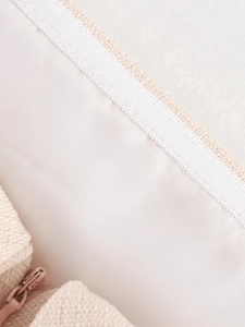 Detail of off-white woven fabric texture and smooth zipper on a minimalist handbag