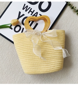 Detail of yellow woven straw tote bag with heart wooden handle and white tulle ribbon bow