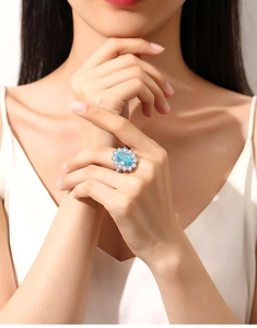 Detailed view of an oval blue gemstone ring with diamond halo on model's hand