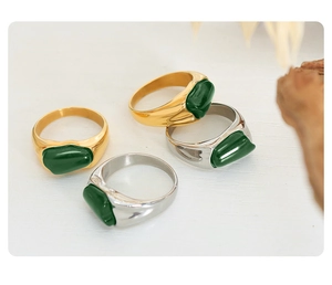 Detail of vintage gold and silver rings with irregular green enamel inlays on white surface