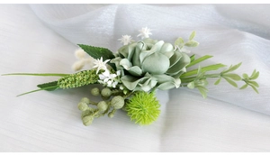 Detailed view of dusty green faux rose boutonniere with white accents on silk fabric