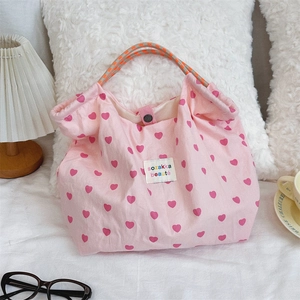 Detailed close-up of a pink canvas tote bag with red heart patterns and woven orange handles