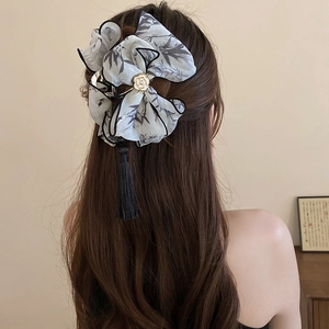 Détail de la pince à cheveux avec nœud en soie, rose dorée et pompons noirs