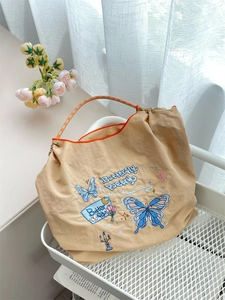 Detail of colorful butterfly embroidery and Butterfly Poetry text on a beige tote bag