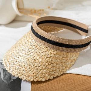 Detail of straw sun visor with black and brown striped ribbon on a wood texture