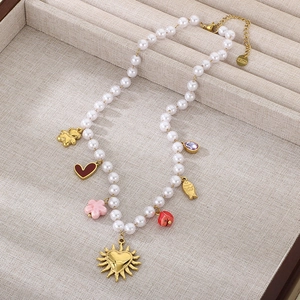 Detail of pearl necklace featuring gold heart, floral, and colorful enamel charms on a tray