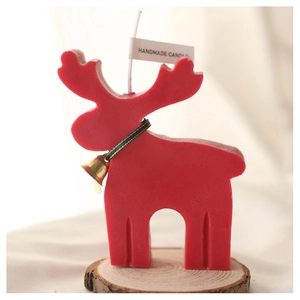 Detail of a red reindeer-shaped candle with a gold bell and handmade tag on wood