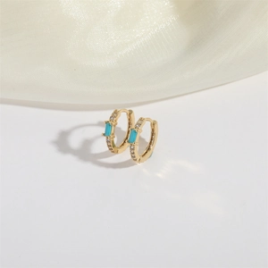 Detail of gold huggie earrings with a rectangular turquoise stone and clear crystals
