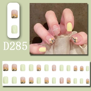 Press-on nail set with yellow tulip designs and pearl accents on pastel green base