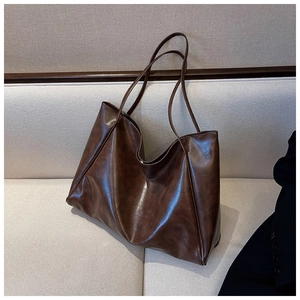 Detail view of large dark brown soft leather tote bag on a white fabric sofa