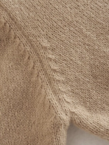 Detailed macro view showing the soft beige knit fabric texture and shoulder seam craftsmanship